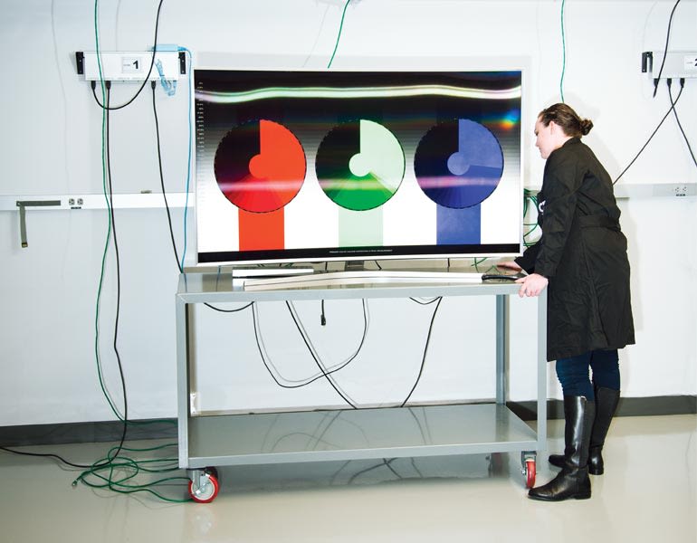 A TV tester wheeling a 4K HDR TV into a CR TV lab.