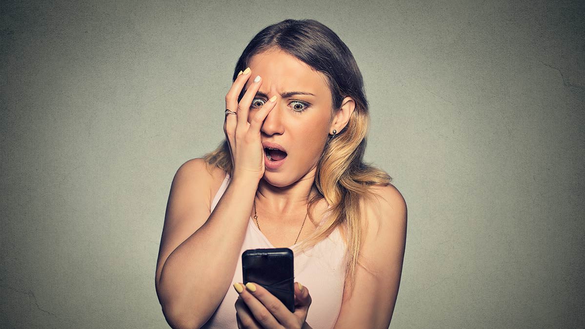 A horrified woman looking at her smartphone. 