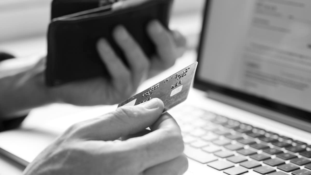 A hand holding a credit card in front of a laptop. 