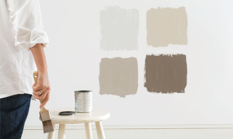 A woman standing back, assessing four test patches of paint to see which color she likes. 